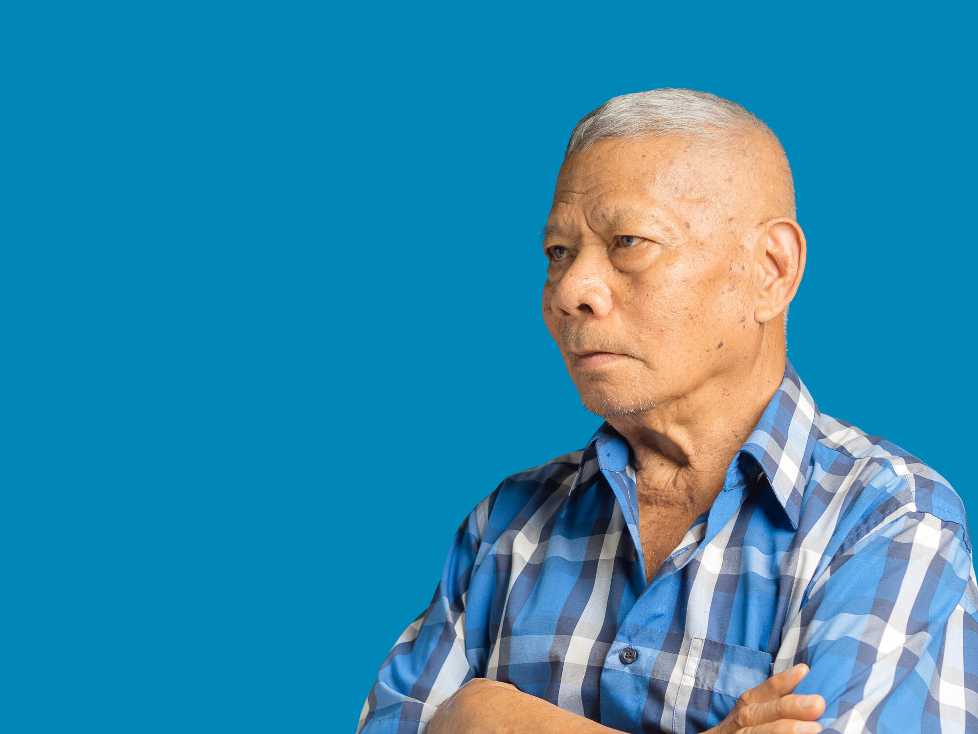 An elderly Asian man in a blue shirt arms crossed and looking aw An elderly Asian man in a blue shirt arms crossed and looking aw