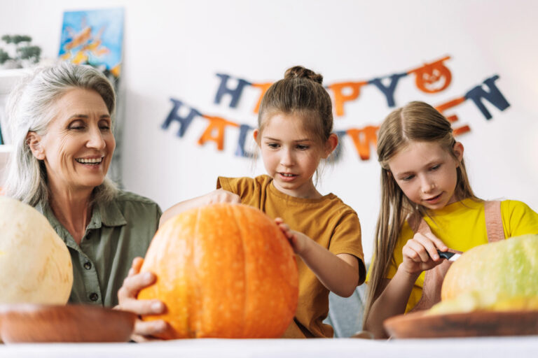 Smiling, senior woman and two little, cute girls carving pumpkins for halloween celebration Smiling, senior woman and two little, cute girls carving pumpkins for halloween celebration