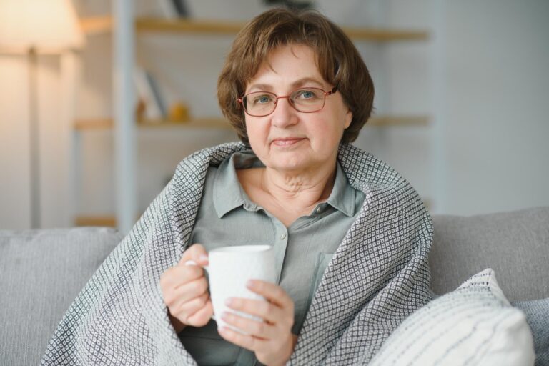 Smiling mature elder 65s woman sitting relaxing with cup of tea, coffee. Senior mid age stylish look woman with eyeglasses portrait with cup looking away at modern home Smiling mature elder 65s woman sitting relaxing with cup of tea, coffee. Senior mid age stylish look woman with eyeglasses portrait with cup looking away at modern home