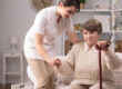 Senior,Disabled,Woman,Standing,Up,With,Carer's,Help