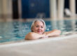 Smiling senior woman enjoying relaxation in an indoor swimming pool, leaning on the poolside. Concept of active lifestyle, wellness, health, hydrotherapy, and leisure for older adults.