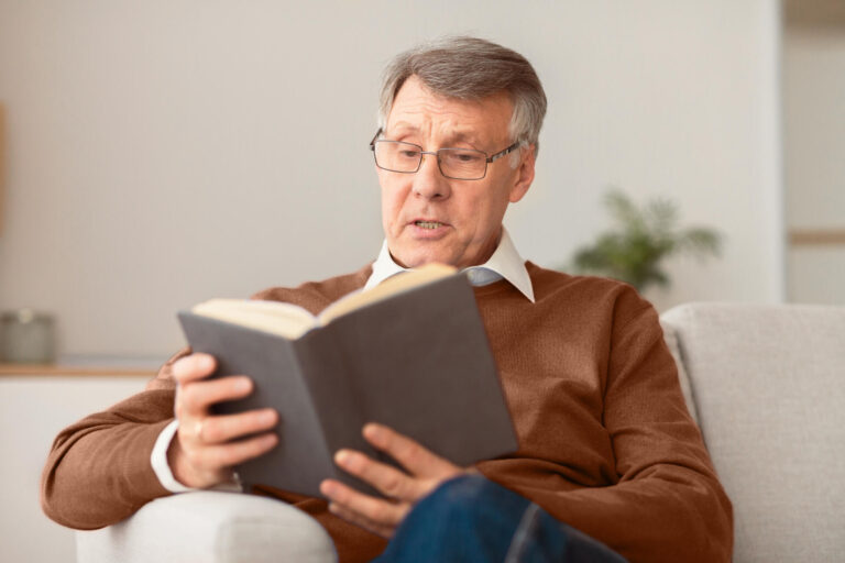 Retired man reading book sitting on couch at home