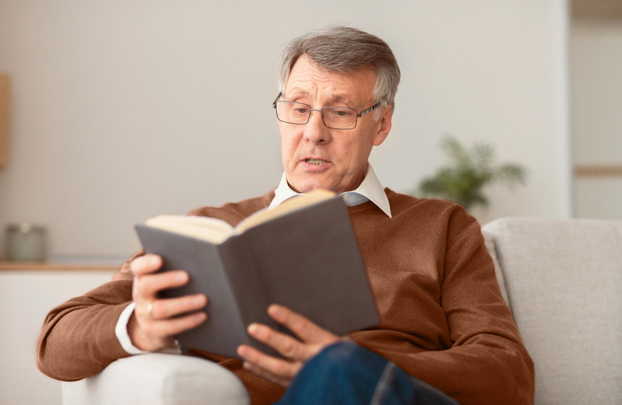 Retired man reading book sitting on couch at home