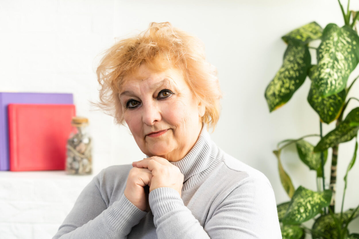 Smiling middle aged mature grey haired woman looking at camera, happy old posing at home indoor, positive single senior retired female sitting on sofa in living room headshot portrait