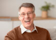 Senior Man Laughing At Camera Sitting On Couch At Home