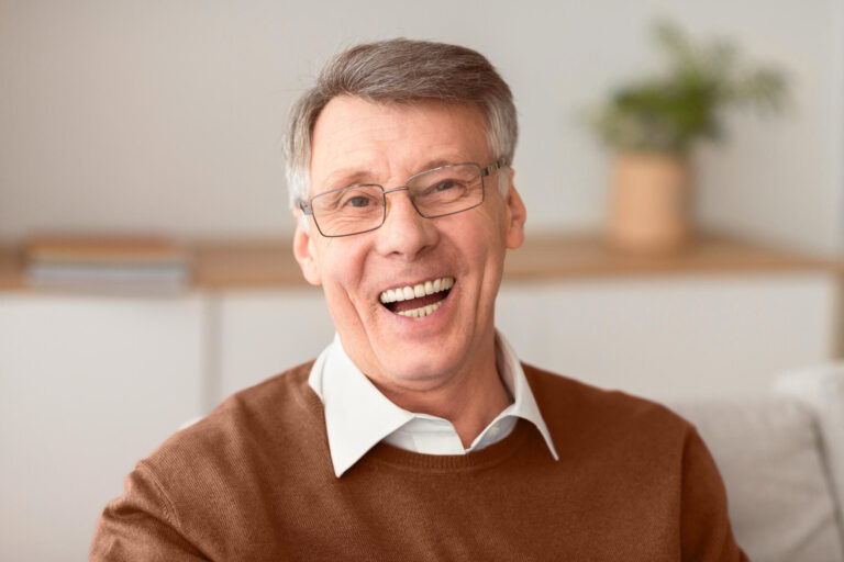 Senior Man Laughing At Camera Sitting On Couch At Home