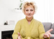 Smiling middle aged mature grey haired woman looking at camera, happy old lady posing at home indoor, positive single senior retired female sitting on sofa in living room headshot portrait