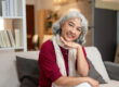 A portrait of a happy, healthy retired Asian woman at home, sitting on a sofa.