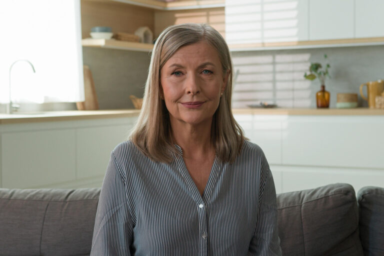 Happy smiling mature retired 70s Caucasian woman mother healthy grandmother gray haired pensioner posing looking at camera. Old elderly senior lady female mortgage couch at home rent house household