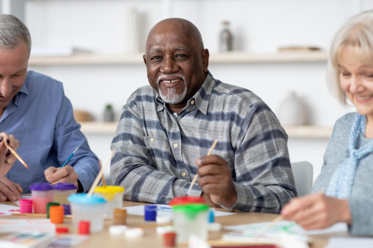 Happy senior black man enjoying painting activity with his friends
