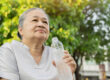 Old Asian woman drinks water after walking exercise in the park.