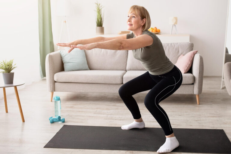 Home training concept. Active mature lady doing squats on yoga mat indoors, copy space