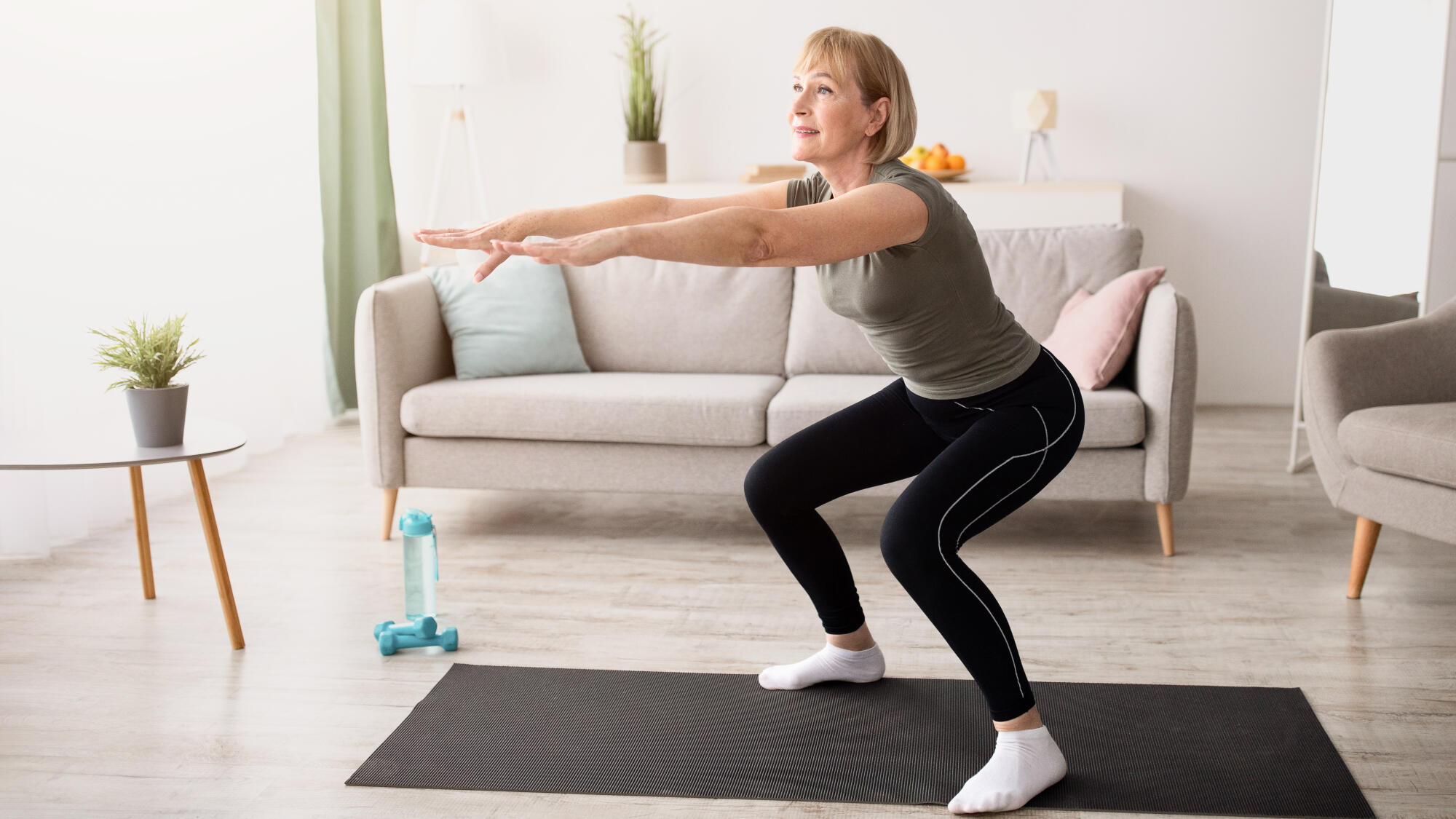 Home training concept. Active mature lady doing squats on yoga mat indoors, copy space
