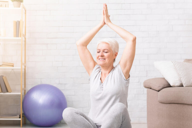Calm senior woman practicing yoga at home with laptop