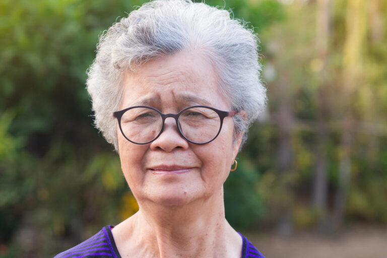 Senior Asian woman looking at camera while standing in a garden