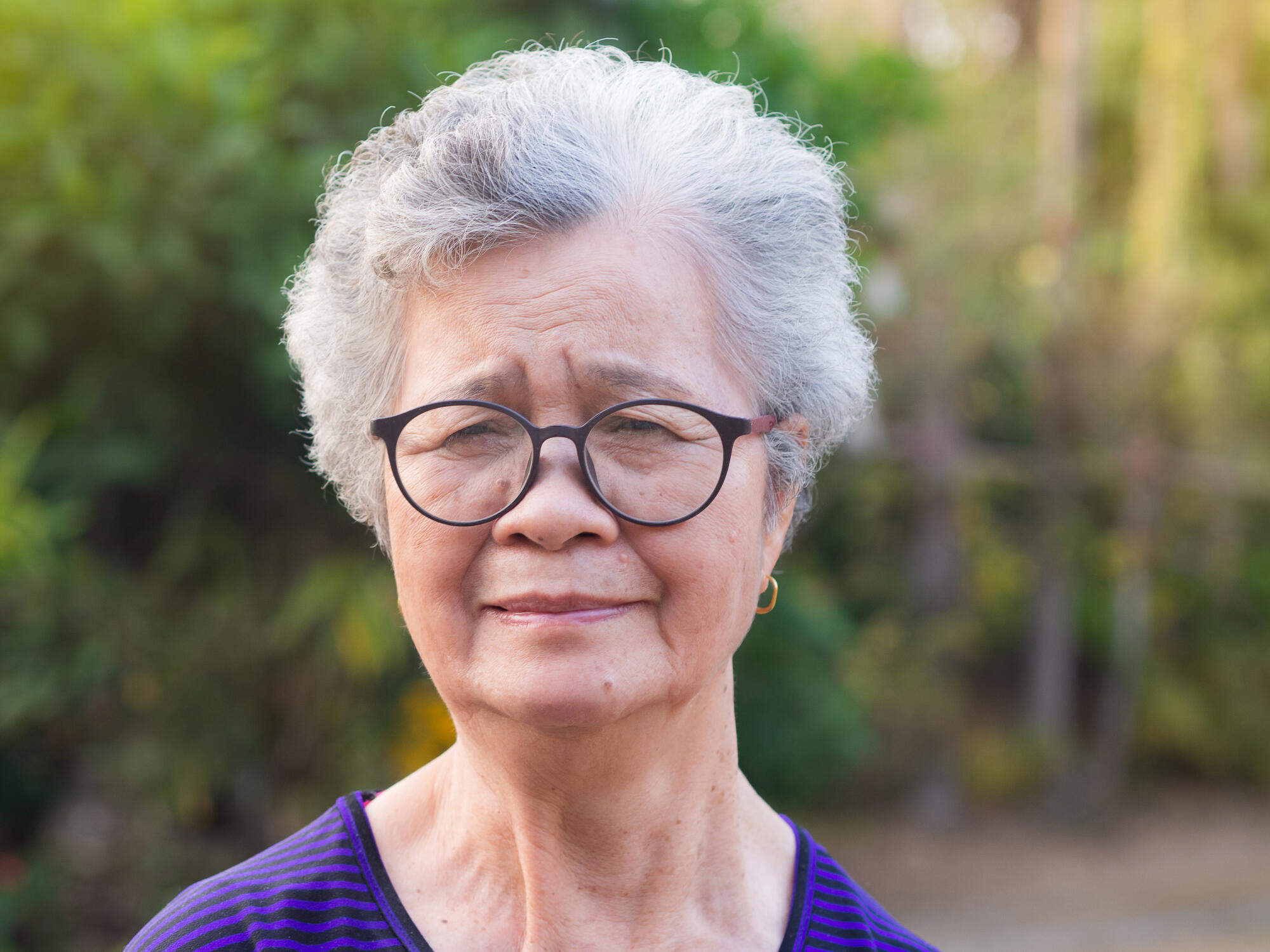 Senior Asian woman looking at camera while standing in a garden