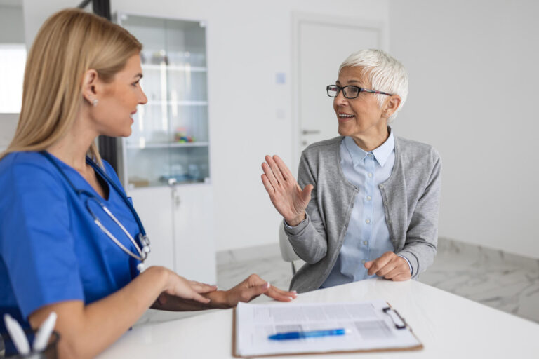 Young woman doctor or GP in white medical uniform consult senior female patient in private hospital. Female therapist speak talk with woman client on consultation in clinic.
