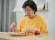 Senior Asian woman enjoying breakfast with toast and jam in cozy kitchen setting, health conscious lifestyle, natural lighting, and simple tableware