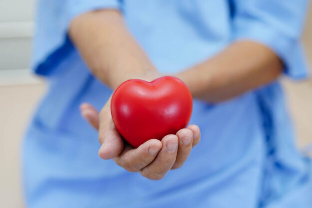 Asian elder senior woman patient holding red heart in hospital.