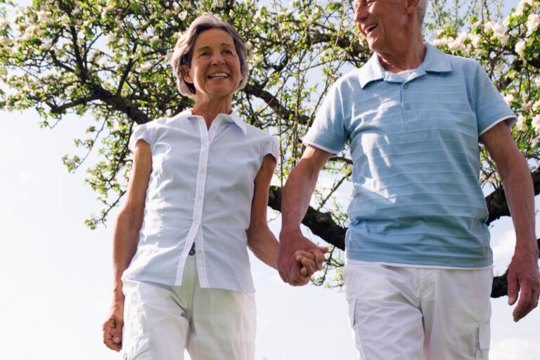 Senior,Couple,Holding,Hands,And,Walking,Through,A,Field,Of